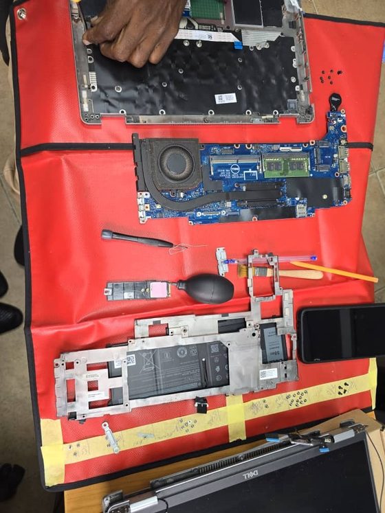 A Hankaka Technologies engineer dismantling a business notebook on a red field ESD mat at a client office, with the keyboard, system board, heatsink, battery and storage laid out in order for an onsite part replacement.