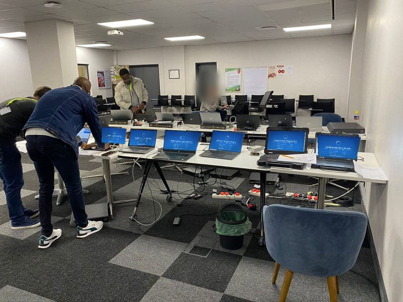 Des ingénieurs de Hankaka Technologies réalisent une inscription Windows Autopilot sur une rangée d’ordinateurs portables installés sur des tables de préparation temporaires, lors du renouvellement du parc d’un client. Les éléments identifiants sont masqués.